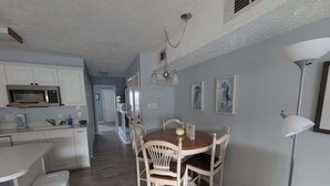 A kitchen with white cabinets, a dining table with chairs, a trash bin, and a pendant light. - Don't Worry. Beach Happy! (Carolina Beach)