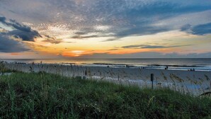 Una playa con un atardecer, un primer plano con hierba y vista al océano.