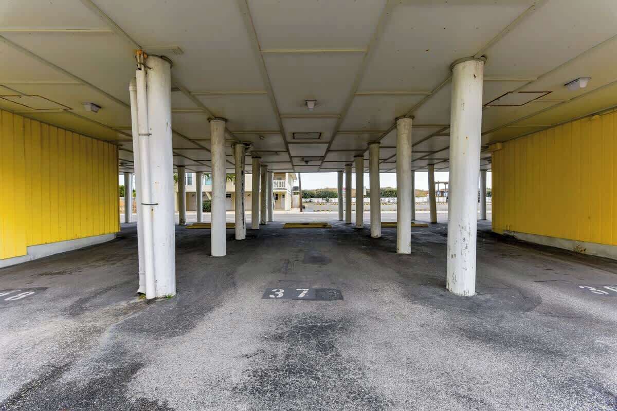 An indoor parking area with white pillars, yellow walls, and a concrete floor with parking space numbers.