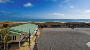 Una propiedad frente a la playa con un edificio de techo verde, una zona arenosa y el océano al fondo.