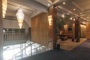 Eine Hotelhalle mit Treppe, Sitzgelegenheit und Rezeption.