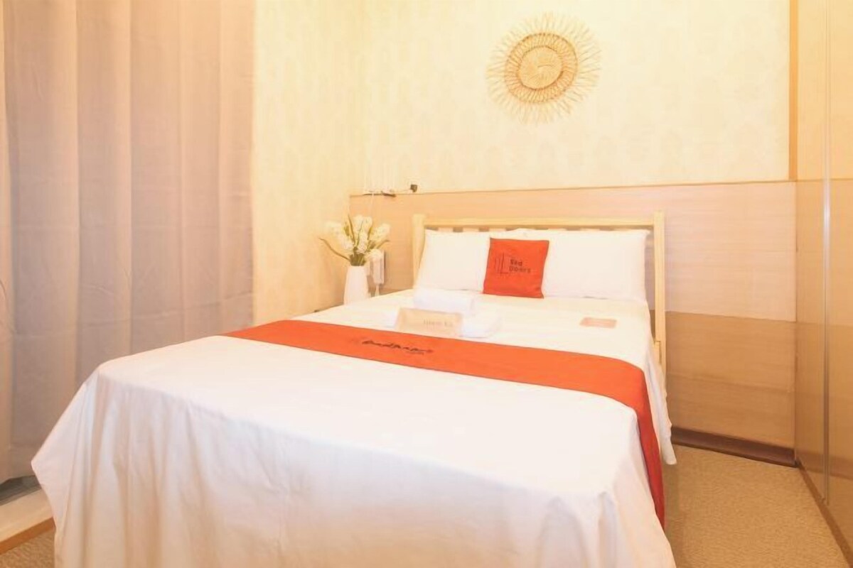 Une chambre d’hôtel avec un lit soigneusement fait, une petite table sur laquelle est posé un vase de fleurs et un objet décoratif fixé au mur.