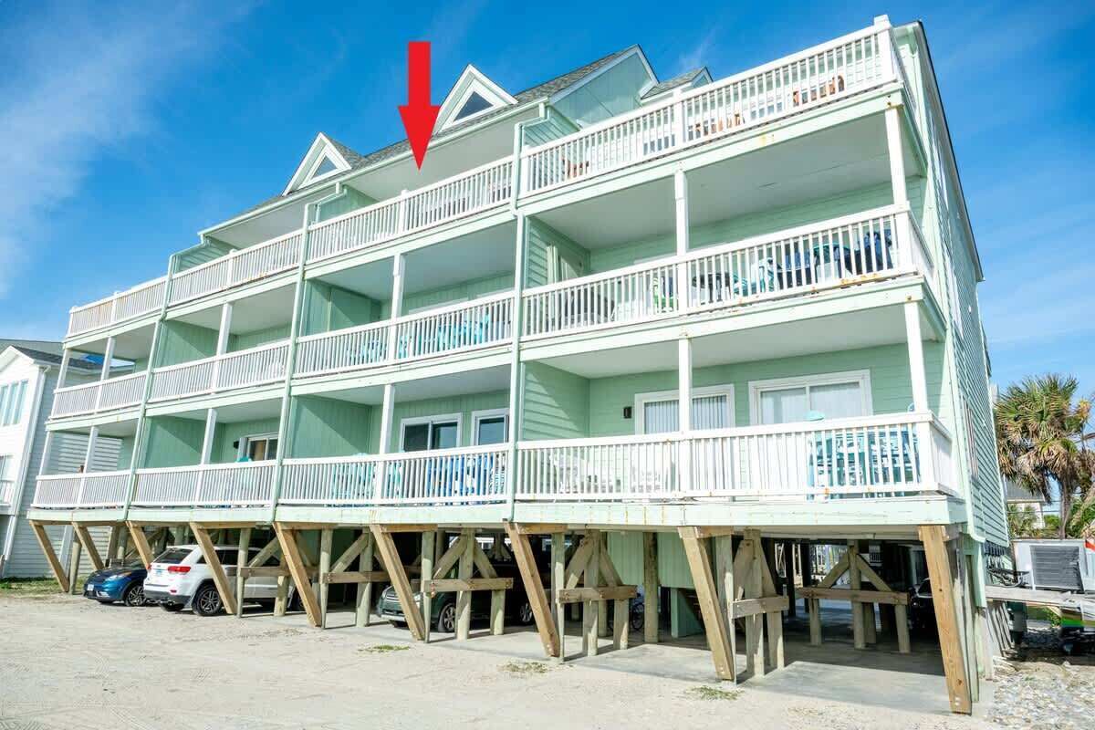 A multi-story beachfront building with balconies, a visible downward arrow, and parked cars.