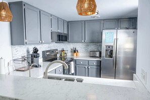 A modern kitchen with grey cabinets, stainless steel appliances, a microwave, toaster, and a refrigerator.