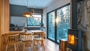 A modern kitchen with a large window, a dining area with wooden chairs, and a wood-burning stove.