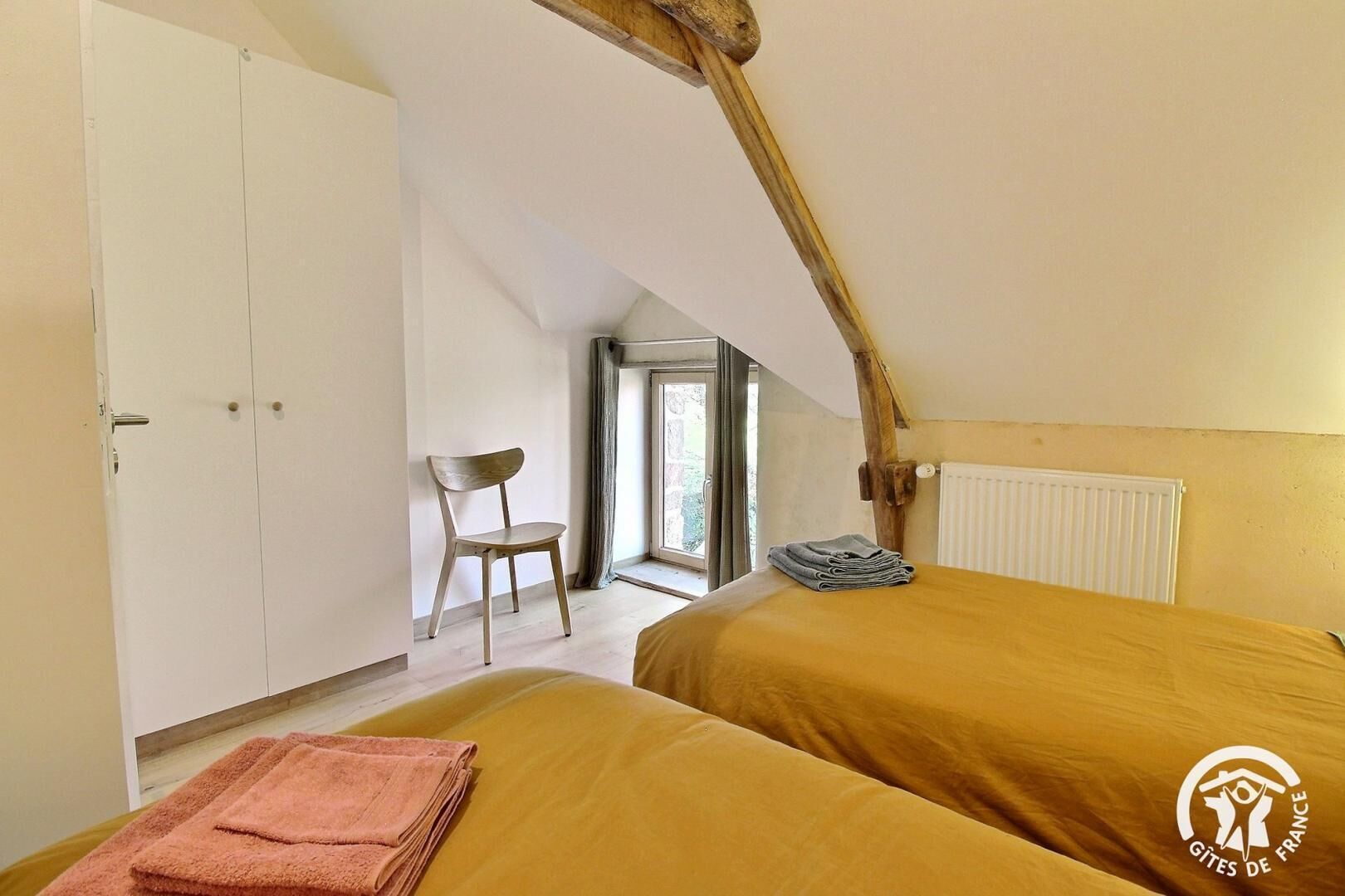 A bedroom with two beds, a wooden chair, a radiator, and a window with a view.