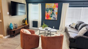A modern living room with a flat-screen TV, two brown armchairs, a grey sofa, and a colorful abstract painting. - Stylish Cozy 2-bedroom Duplex  in enjoyable Stafford with WiFi, AC, Smart TVs (Stafford)