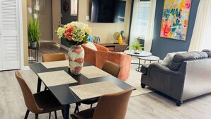 A modern living room with a dining area, a gray sofa, and a TV mounted on the wall. - Stylish Cozy 2-bedroom Duplex  in enjoyable Stafford with WiFi, AC, Smart TVs (Stafford)