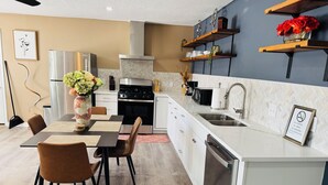 A modern kitchen with a dining area, featuring a stainless steel stove, white cabinets, and a wooden dining table with chairs. - Stylish Cozy 2-bedroom Duplex  in enjoyable Stafford with WiFi, AC, Smart TVs (Stafford)