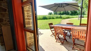 A patio with a table and chairs, an umbrella, and a view of a grassy area. - Le Tejtal 6pers - PLUMERGAT (PLUMERGAT)