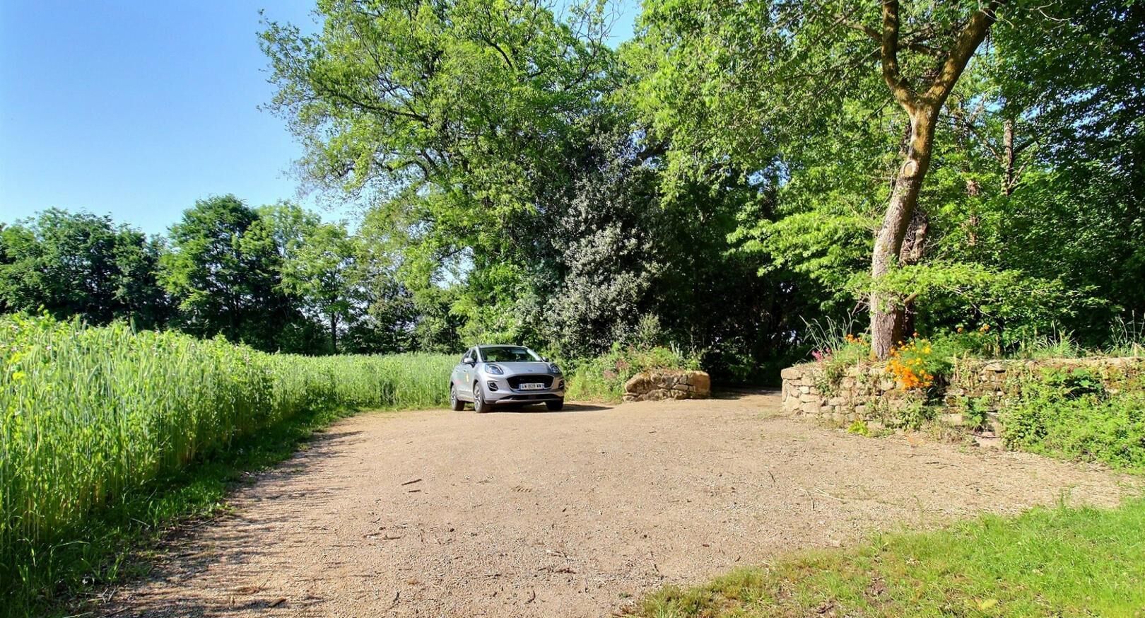 Un chemin de gravier avec une voiture garée sur le côté, entouré de verdure et d’arbres.