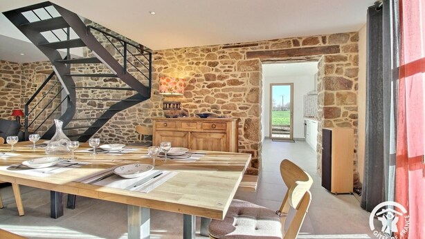 A dining area with a wooden table set for four, a stone wall, and a modern staircase. - Le Tejtal 6pers - PLUMERGAT (PLUMERGAT)
