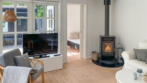 A cozy living room with a flat-screen TV, a sofa, a chair, a white table, and a wood-burning stove. - Stunning home in Hals with WiFi (Hals)