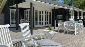 A covered outdoor seating area with white chairs and tables, a small plant on a table, and a wooden deck. - Stunning home in Hals with WiFi (Hals)