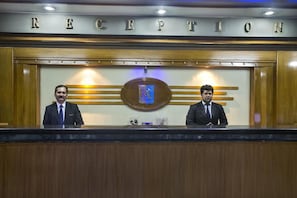 A reception area with a wooden reception desk, two staff members, and a sign above that reads 'RECEPTION'. - Agrabad Hotel (Chittagong)