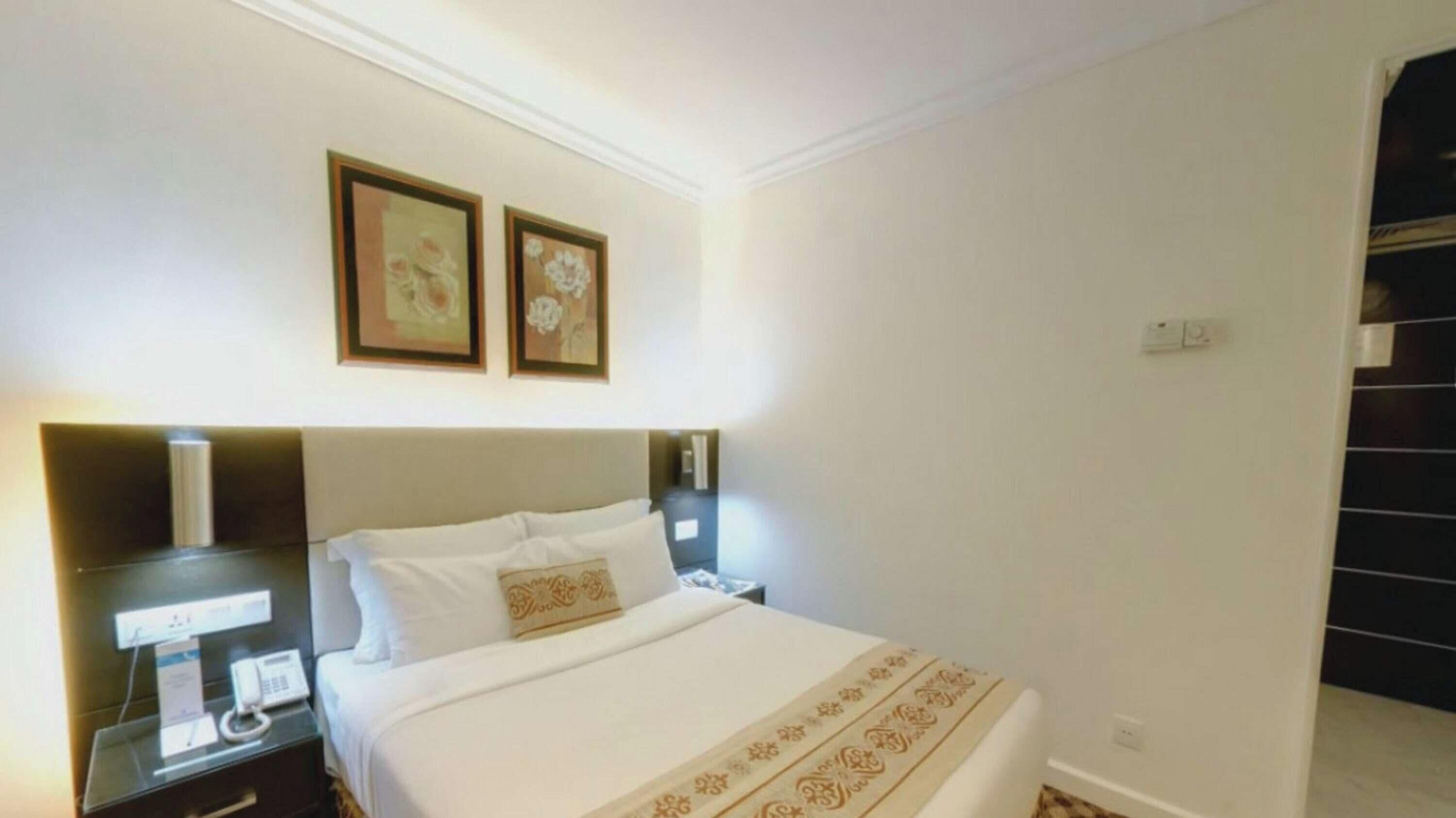 Ein Hotelzimmer mit einem Bett, Nachttischen, einem Telefon und zwei gerahmten Bildern an der Wand.