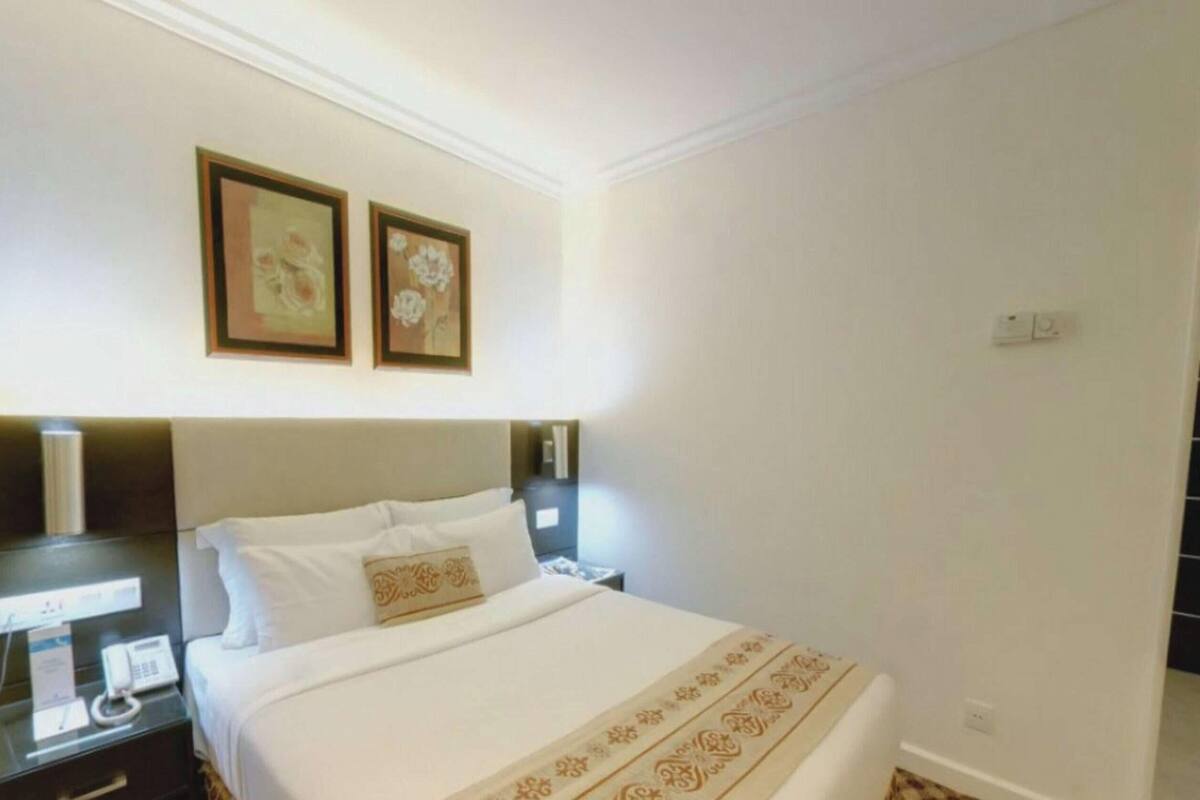 Habitación de hotel con cama, mesitas de noche, teléfono y dos cuadros en la pared.