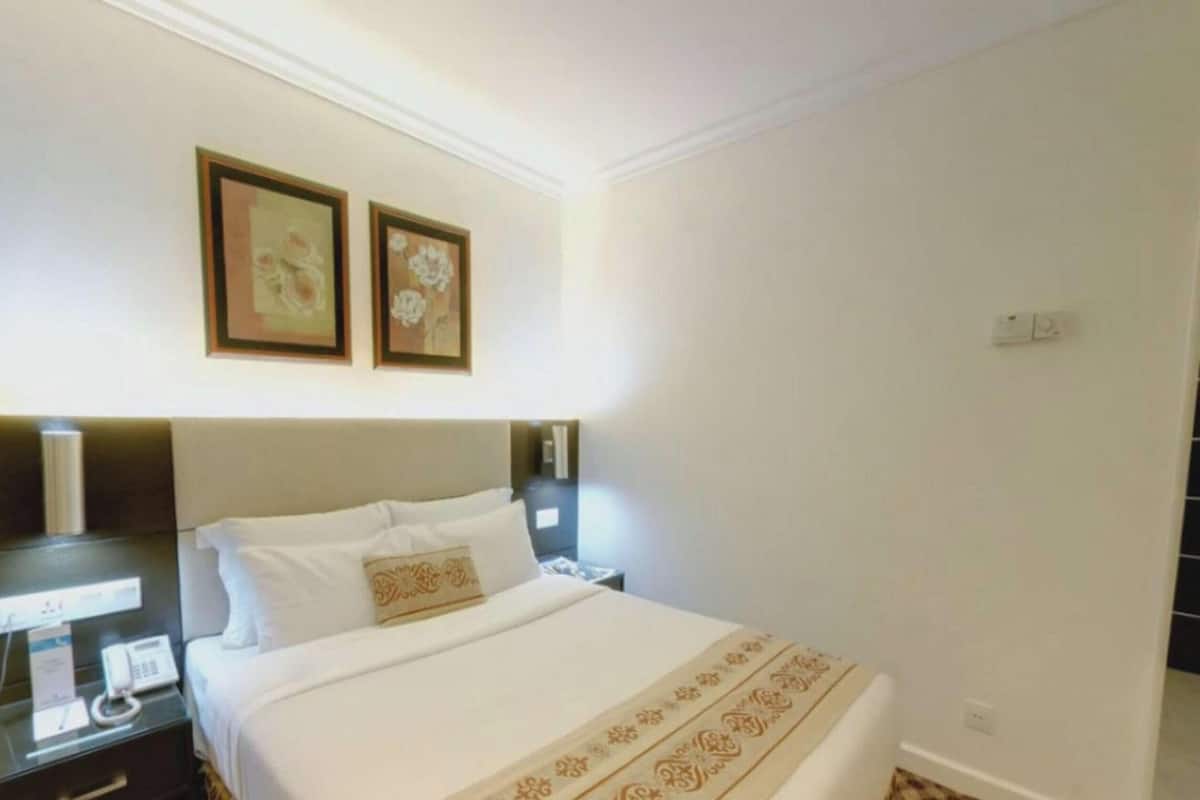 Ein Hotelzimmer mit einem Bett, Nachttischen, einem Telefon und zwei gerahmten Bildern an der Wand.