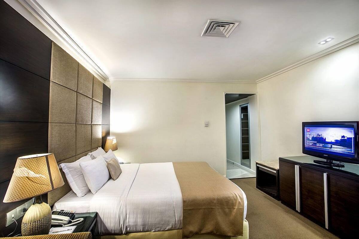 Una habitación de hotel con cama, televisión, lámpara, teléfono y escritorio.