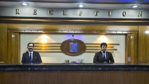 A reception area with a wooden reception desk, two staff members, and a sign above that reads 'RECEPTION'. - Agrabad Hotel (Chittagong)