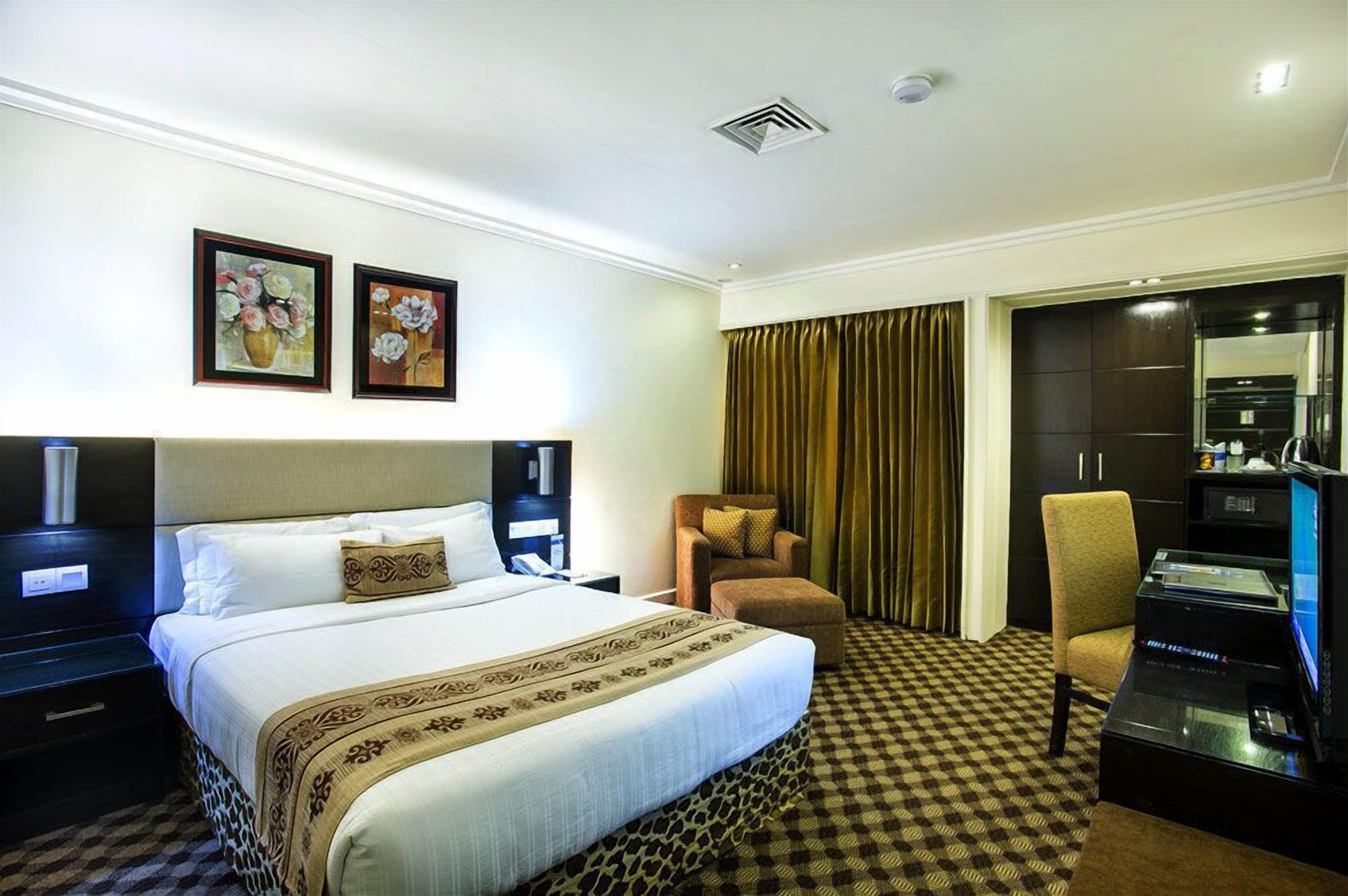 Ein Hotelzimmer mit einem großen Bett, zwei gerahmten Kunstwerken, einem Schreibtisch mit Computer, einem Sessel und einem Kleiderschrank.