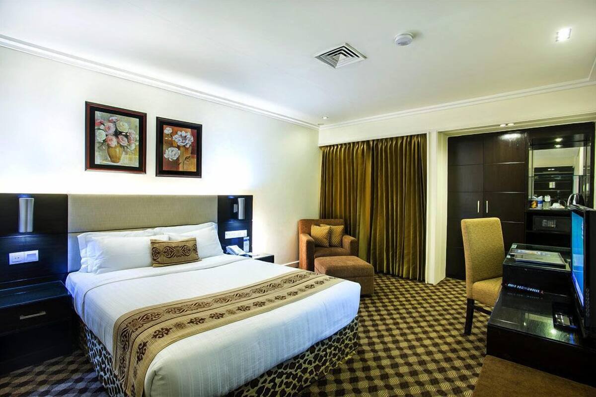 Una habitación de hotel con una cama grande, dos cuadros enmarcados, un escritorio con computadora, una silla y un armario.