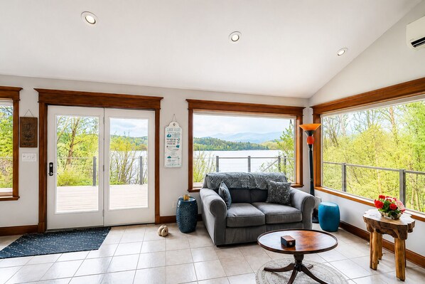 Amplia habitación con un ventanal, un sofá, una mesa de centro y vistas a un lago.