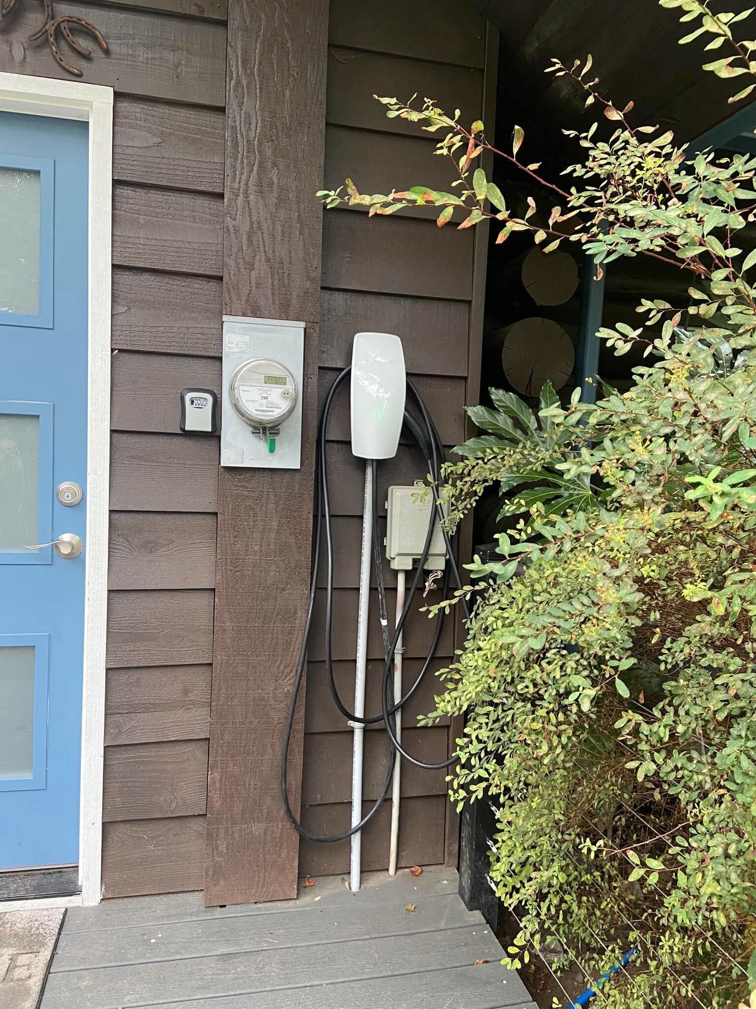 An outdoor electrical box with a meter and a white device, possibly a thermostat, mounted on a wooden wall.