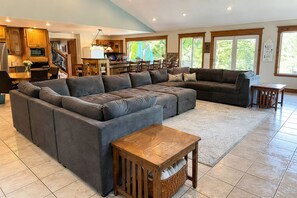 Amplia sala de estar con un sofá seccional grande, una mesa de centro de madera y una zona de cocina con armarios de madera y una mesa de comedor.