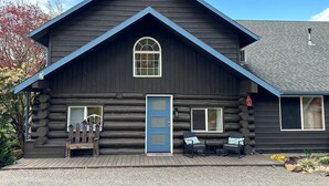 A log cabin with a blue door, a small porch with a bench, and a window with a view of the surrounding area. - Mayfield Lake Waterfront Escape (Mossyrock)
