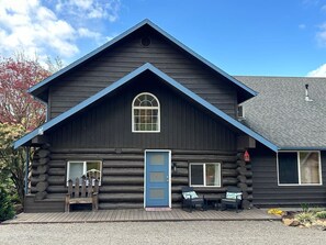 A log cabin with a blue door, a small porch with a bench, and a window with a view of the surrounding area.