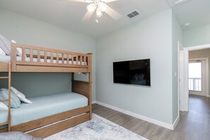 A bedroom with a bunk bed, a ceiling fan, a mounted TV, and a view to another room.