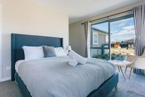 A modern hotel room with a large bed, a chair, and a view of a residential area through a sliding glass door. - Snowflake Tekapo (Lake Tekapo)