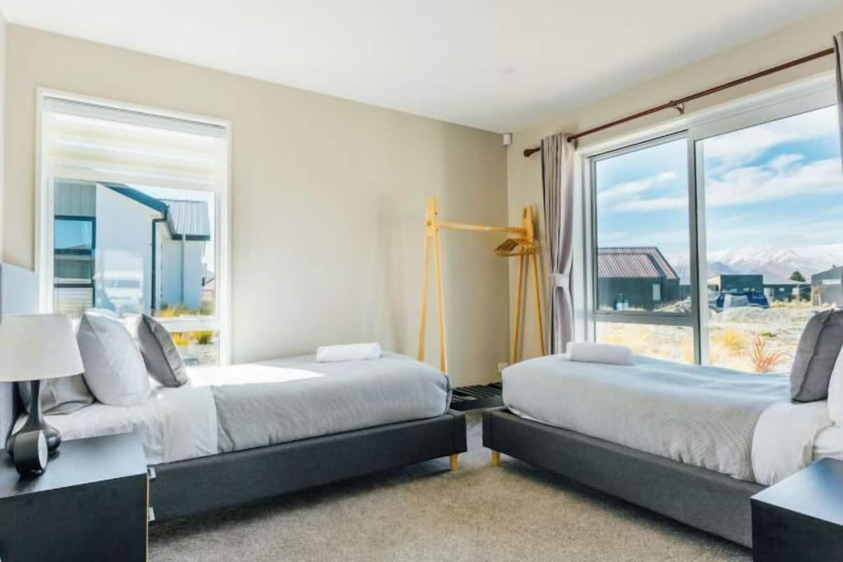 A modern bedroom with two beds, a large window, and a view of a mountainous landscape.