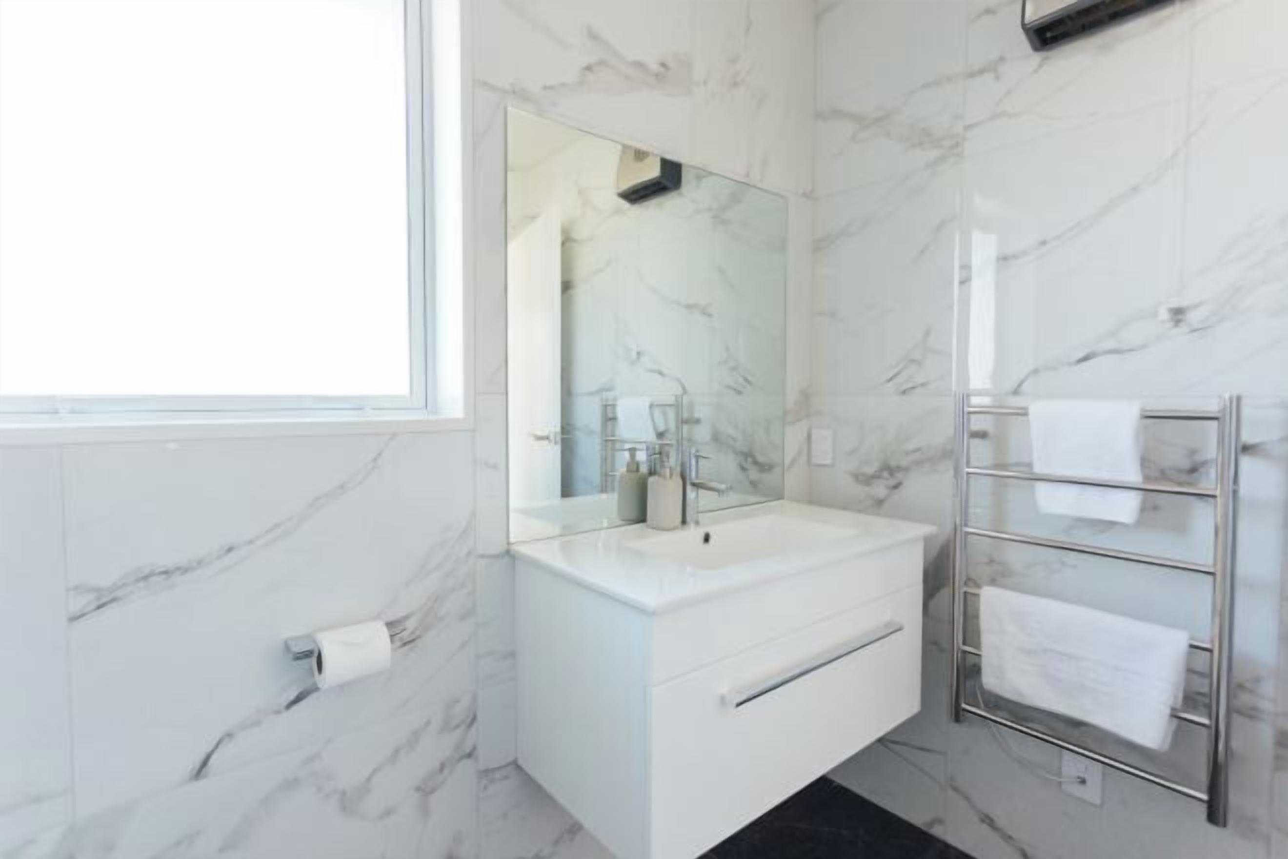 Un baño moderno con pared de mármol, un lavamanos blanco, un espejo grande y un perchero para toallas.
