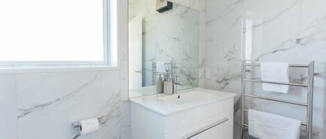 Un baño moderno con pared de mármol, un lavamanos blanco, un espejo grande y un perchero para toallas.