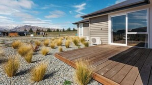 Ein modernes Haus mit einer Holzdiele, großen Schiebegläsern und einem Kiesgarten mit Rasen.