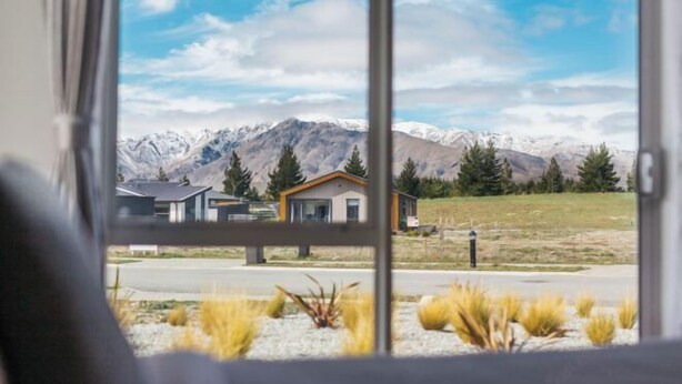 Blick durch ein Fenster auf ein modernes Haus mit Bergblick.