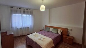 Un dormitori amb un llit de fusta, una taula de nit, cortines translúcides i una làmpada penjant.