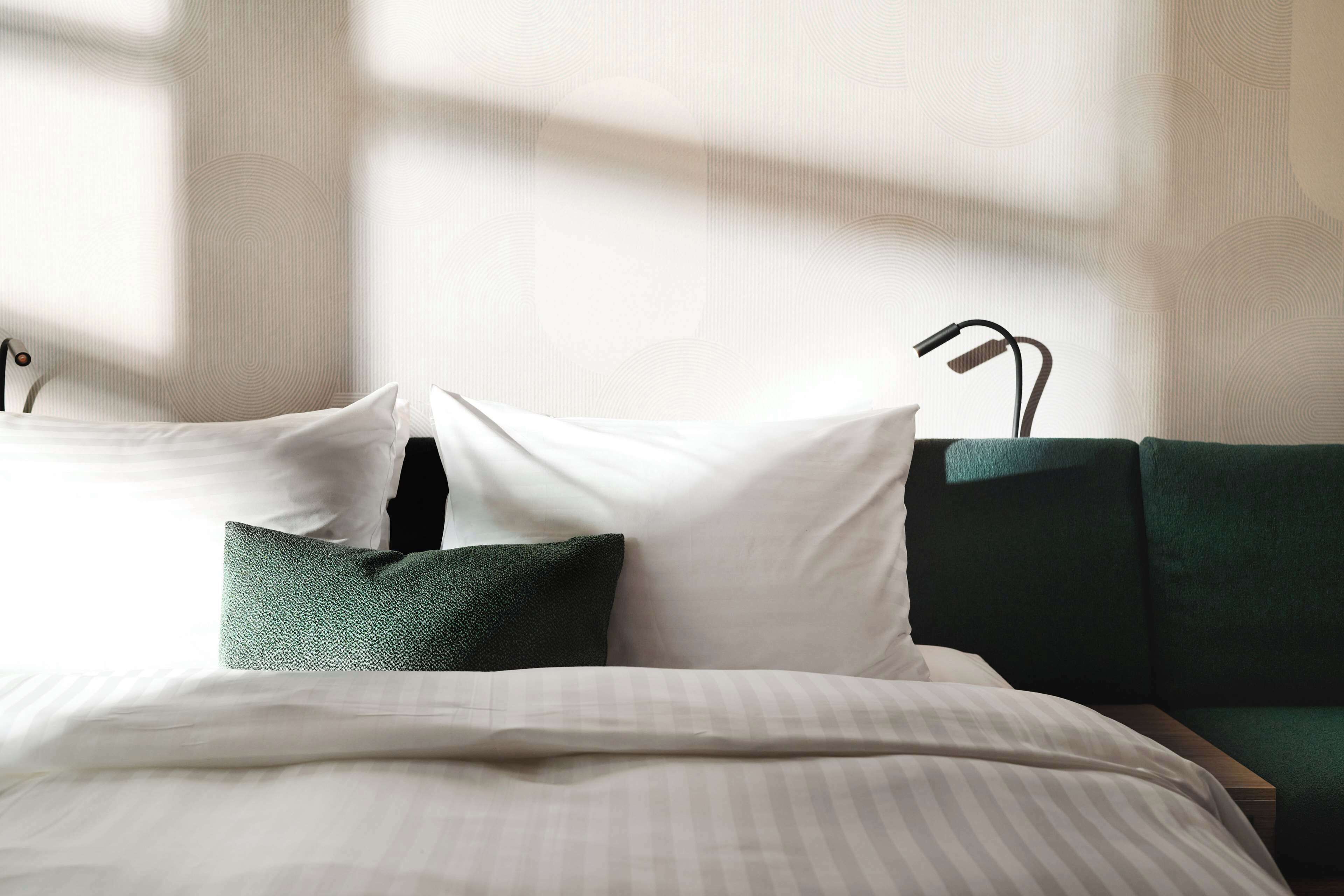 Ein ordentlich gemachtes Bett mit weißen und grünen Kissen, einer gestreiften Decke und einem mit grünem Stoff bezogenen Kopfteil.