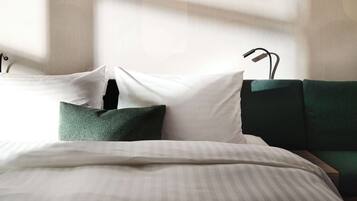 Ein ordentlich gemachtes Bett mit weißen und grünen Kissen, einer gestreiften Decke und einem mit grünem Stoff bezogenen Kopfteil.