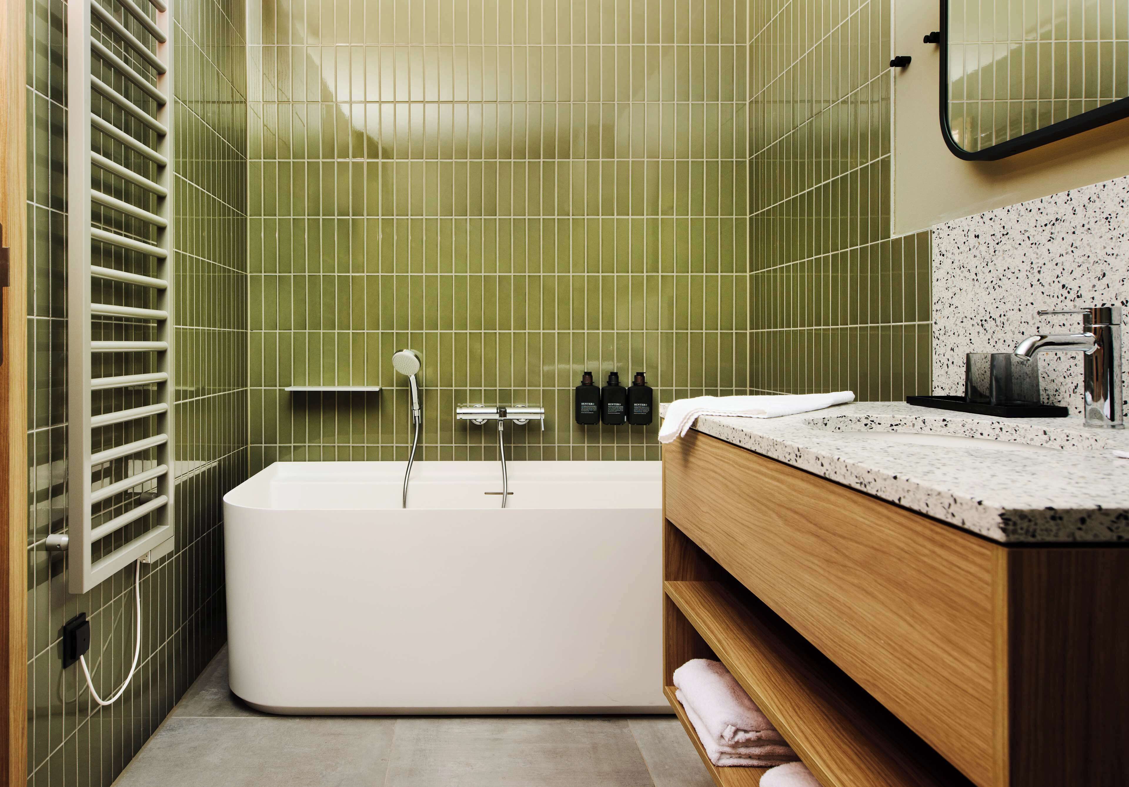 A modern bathroom with a freestanding bathtub, a wooden vanity, and a tiled wall.