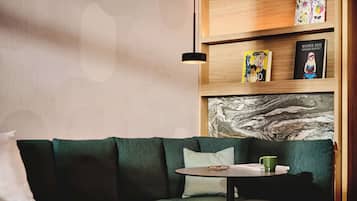 A modern living room with a green sofa, a small round table with a green mug, and a bookshelf with books and decorative items.