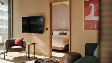 A modern hotel room with a bed, a TV, a seating area with a chair and a small table, and a large window.