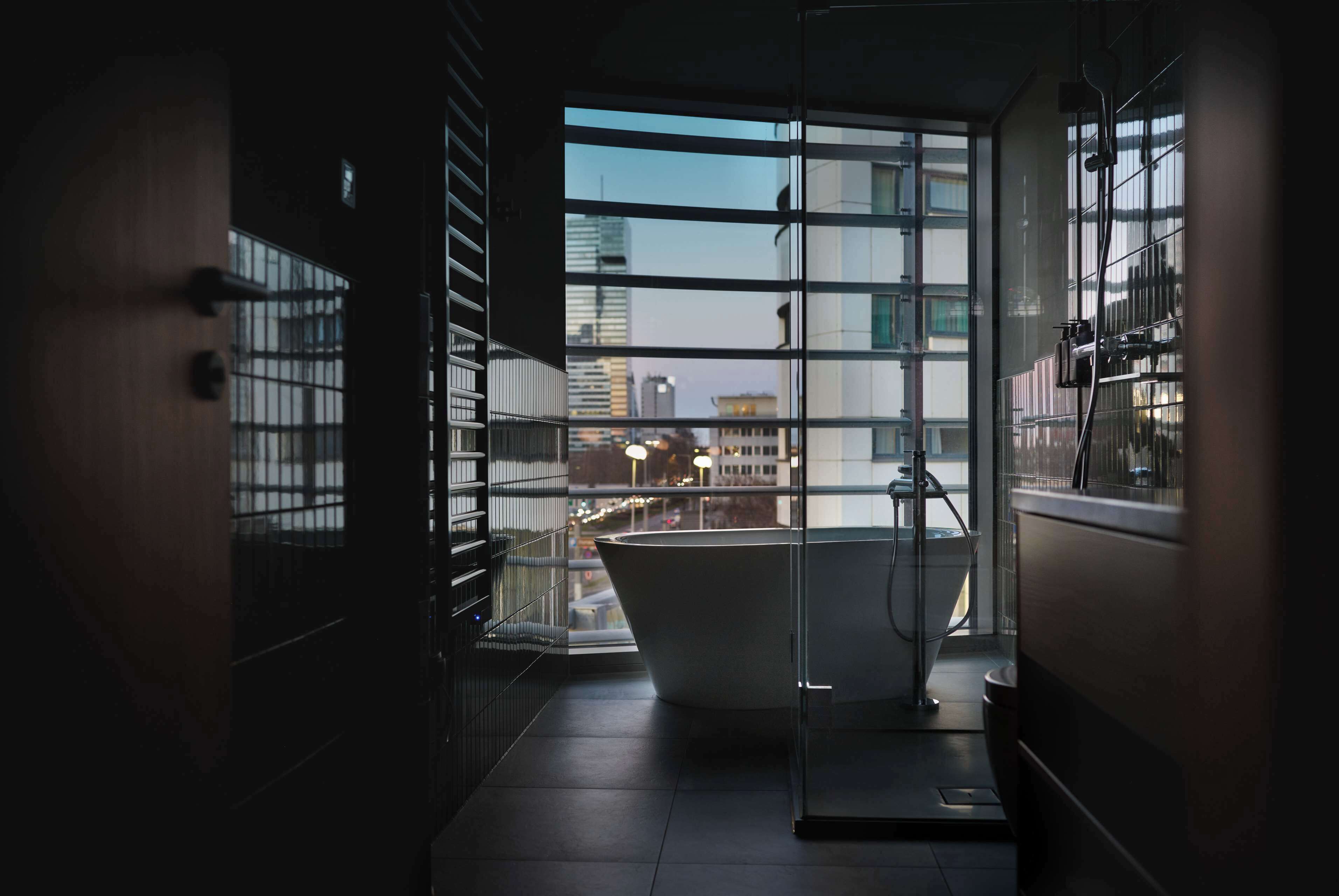 A modern bathroom with a large bathtub, a glass shower enclosure, and a view of the cityscape through large windows.
