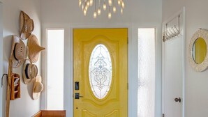 En knallgul dörr med ett dekorativt glasfönster, en träbänk och en hängande lampa.
