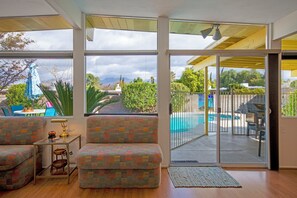 Una sala de estar con un amplio ventanal corredizo que da a un patio trasero con piscina.