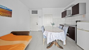A compact living space with a dining table, sofa, kitchenette, and a door leading to another room.