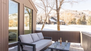 Une terrasse avec un canapé et une table, de grandes fenêtres et une vue sur un paysage enneigé.
