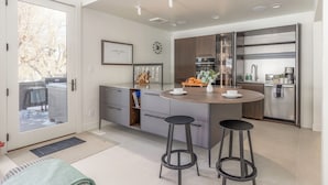 Une cuisine moderne dotée d’un îlot central, de tabourets de bar, d’un four encastré et d’une grande fenêtre.